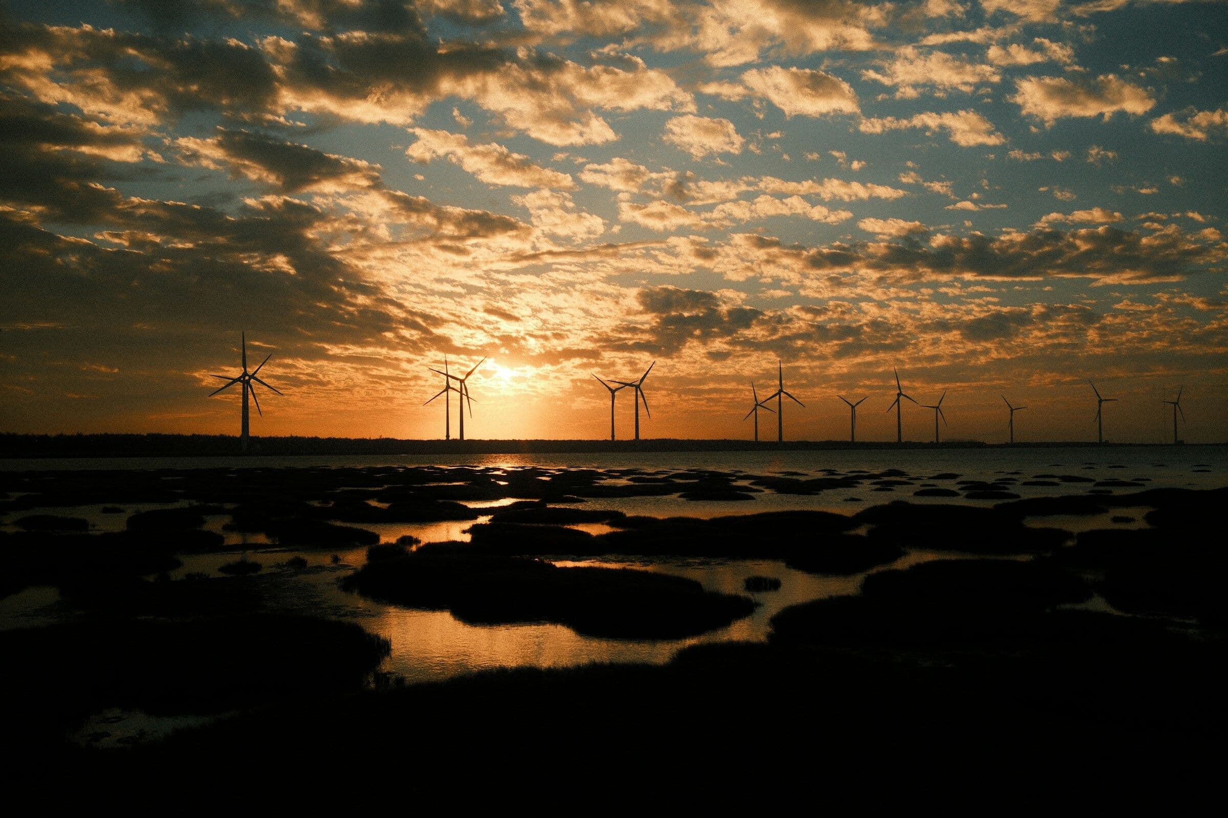 Wind turbines at sunset seen across a tidal marsh